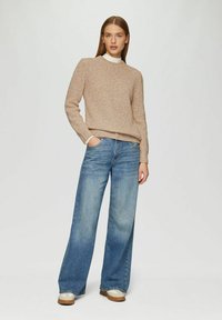 Beiger gerippter Pullover mit Rundhalsausschnitt, kombiniert mit weiten blauen Jeans. Braune und weiße Schuhe runden das Outfit ab.