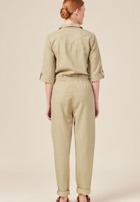 Olijfgroen jumpsuit met een kraag, opgerolde mouwen, een elastische tailleband en taps toelopende pijpen van een zachte, gestructureerde stof.