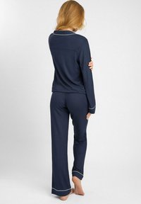 Granatowy zestaw piżamowy z długimi rękawami i spodniami, wykonany z miękkiego materiału. Posiada białą lamówkę przy kołnierzyku i mankietach, luźny krój.