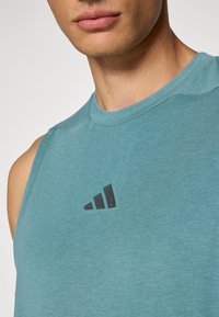 Sleevless teal træningsbluse lavet af blødt stof, med en rund halsudskæring og et sort Adidas-logo på brystet.