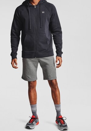 Svart zip-up hoodie med huva, grå shorts och svarta/röda träningsskor. Har mjukt tyg och en logotyp på bröstet.