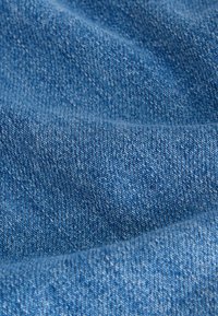 Gros plan sur un tissu en denim bleu montrant un tissage texturé et de subtils plis dans le matériau.