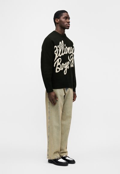 Μαύρο πλεκτό πουλόβερ με κρεμ κείμενο "Billionaire Boys Club", συνδυασμένο με ανοιχτόχρωμο ριγέ παντελόνι και μαύρα και άσπρα παπούτσια.