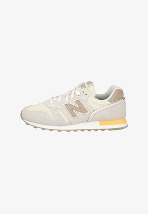 Zapatilla baja beige y crema con paneles de ante y malla, cierre de cordones, cuello acolchado y suela de goma con un detalle amarillo.