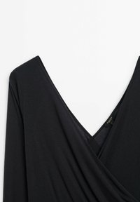 Czarna bluzka typu wrap z głębokim dekoltem w kształcie V i długimi rękawami. Wykonana z miękkiego, lekkiego materiału o gładkim, lekko teksturowanym wykończeniu.