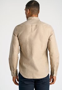 Lichtbeige shirt met lange mouwen, een spitse kraag, subtiele textuur, geruite manchetten en een gebogen zoom. Achteraanzicht, zonder zichtbare patronen.