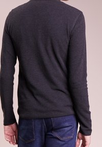 Mörkgrå långärmad tröja med en strukturerad tyg, figurnära design och rundad halsringning. Matchas med blå denimjeans.