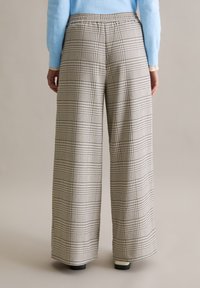 Wijd uitlopende geruite broek in beige en marineblauw, met een elastische tailleband en een zachte stoftextuur. Achteraanzicht toont de algehele snit en het ontwerp.