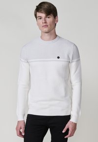 Witte gestructureerde trui met een ronde hals en een contrasterende gladde streep over de borst, met een klein rond logo op de voorkant.