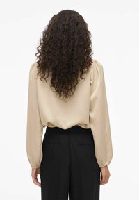 Beige satengbluse med puffede lange ermer, rynkede mansjetter og løs passform, kombinert med svarte høytlivsbukser.