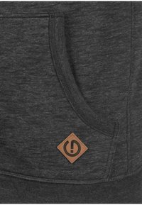 Sudadera de color gris carbón con una tela texturizada, bolsillo tipo canguro y una etiqueta de cuero marrón en forma de diamante.