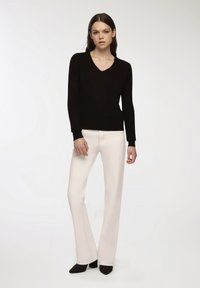 Czarny sweter wykonany na drutach z dekoltem w kształcie litery V i długimi rękawami, zestawiony z białymi spodniami w stylu dzwonów, z wyraźnymi szwami oraz czarnymi szpilkami.