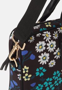 Schwarze Tasche mit floralem Muster, weißen Gänseblümchen, blauen und gelben Akzenten, goldenen Beschlägen und einem dicken verstellbaren Trageriemen. Strukturierter Stoff.