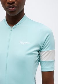 Κοντινό πλάνο ενός ατόμου που φοράει ανοιχτό μπλε φανέλα ποδηλασίας με λευκό φερμουάρ, λογότυπο "Rapha" στο στήθος και λευκή ρίγα στο μανίκι.