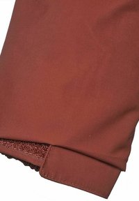 Rustrød stof med en tekstureret finish. Har en elastisk cuff for et tætsiddende udseende og en ren, sømløs kant.