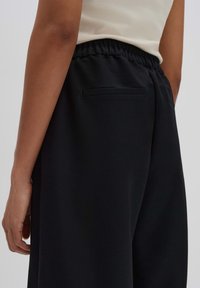 Pantalon de jogging noir avec une taille élastique, doté d'une poche arrière unique et d'une texture lisse en polyester.