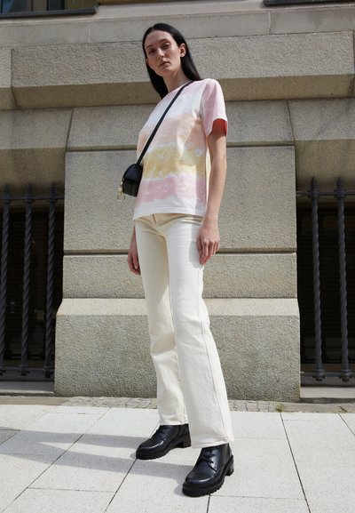 Light pink and cream patterned t-shirt, off-white flared pants, black lace-up boots, and a small black crossbody bag.