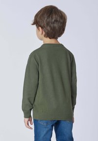 Maglione verde con collo a giro e maniche lunghe, realizzato in un tessuto morbido. Indossato sopra un paio di jeans in denim blu, con polsini e orlo a coste.