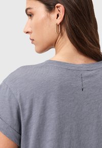 Camiseta gris de manga corta con un corte relajado, que presenta un pequeño logo negro cerca del escote. Tejido suave y texturizado con mangas enrolladas.