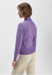 Lila gestrickter Turtleneck-Pullover mit gerippten Bündchen und Saum, der eine taillierte Silhouette aufweist. Glatte Textur vor einem hellen Hintergrund.