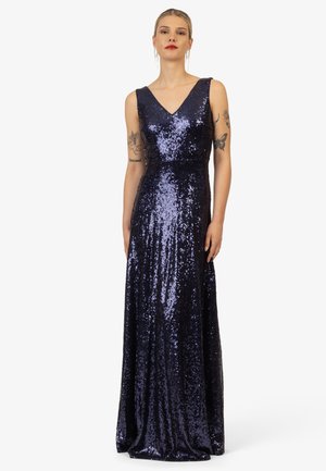Abito lungo da sera blu navy, con scollatura a V, senza maniche e una texture completamente luccicante di paillettes che scintillano, creando una silhouette fluida.