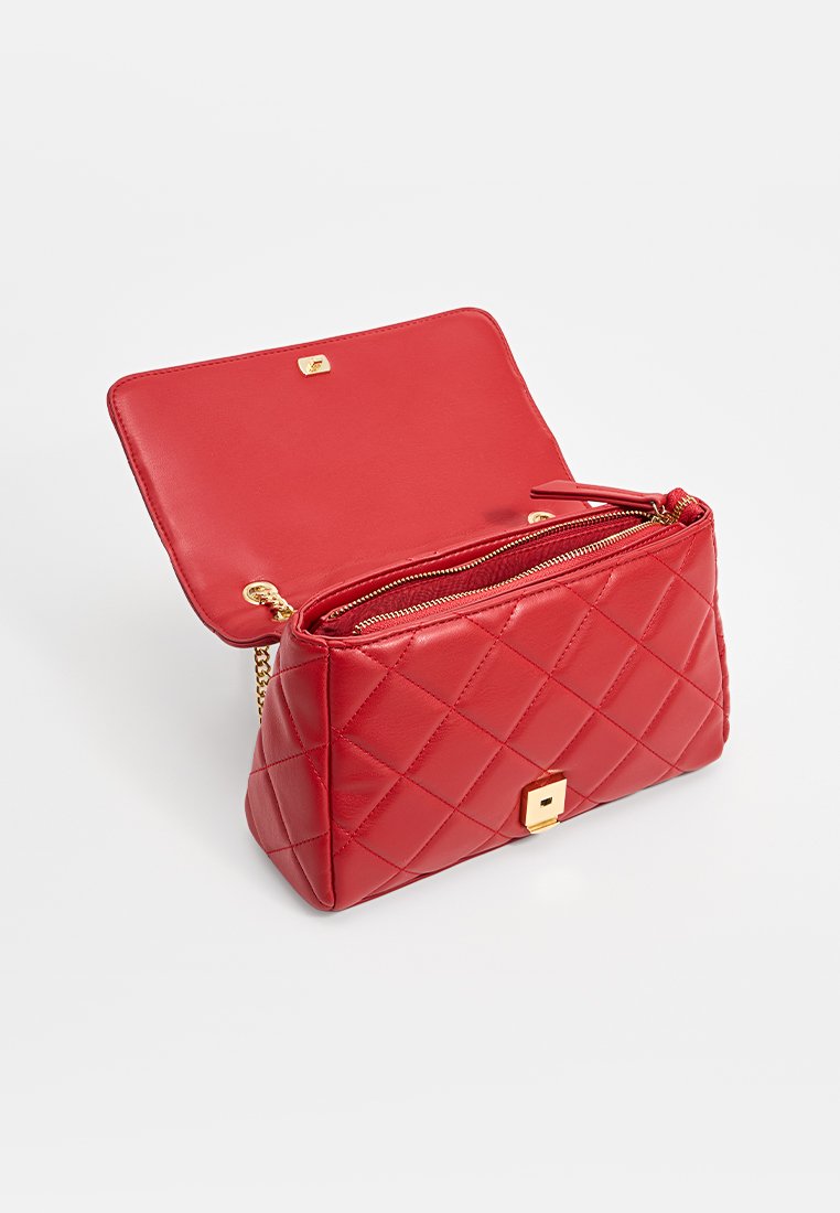 Rote gesteppte Leder-Handtasche mit goldener Schnalle, offenem Deckel und einem Reißverschluss-Innenfach, auf weißem Hintergrund dargestellt.