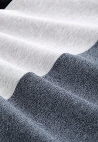 Textilgewebe mit wellenförmigen Falten, das kontrastierende Farben aufweist: sanftes Grau, cremiges Weiß und dunkles Marineblau. Sanfte Textur mit dezenten Mustern.