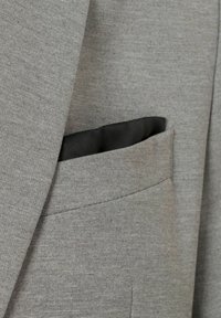 Tissu de blazer gris avec une apparence texturée. Présente une poche latérale avec une doublure sombre. Design ajusté avec des épaules structurées.