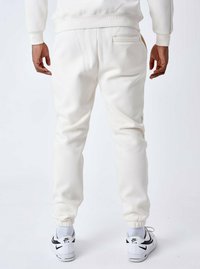 Joggers de felpa blanca con un corte ajustado, que cuentan con un bolsillo trasero y puños elásticos. El modelo lleva zapatillas negras y blancas.