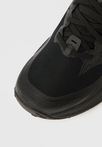 Μαύρο αθλητικό παπούτσι με υφασμάτινο άνω μέρος με υφή, ανθεκτική ελαστική σόλα, εμφανές σύστημα κορδονιών και κομ�ψές λεπτομέρειες σχεδίασης.