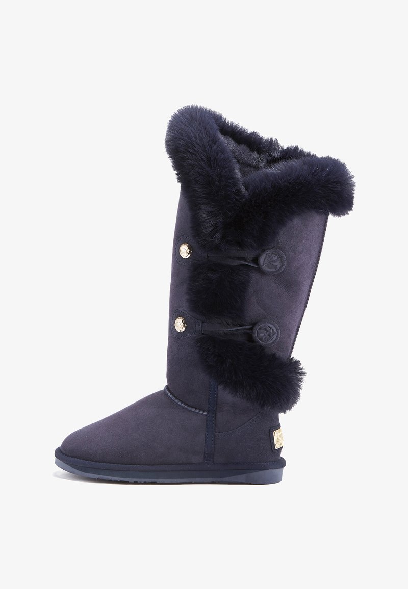 Námornícke modré semišové čižmy po kolená majú plyšový umelý kožušinový okraj, tri dekoratívne gombíky a plochú gumovú podrážku pre lepšiu trakciu.
