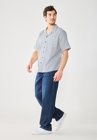 Kurzärmliges Hemd mit blau-weißen verticalen Streifen, zwei Brusttaschen, kombiniert mit lässigen blauen Jeans und weißen Sneakers.