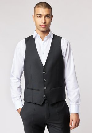 Schwarze Herrenweste mit maßgeschneidertem Design, ausgestattet mit sechs Knöpfen, zwei Fronttaschen und einer glatten Stoffoberfläche, getragen über einem weißen Hemd.