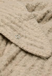 Tissu en laine beige avec une finition texturée, doté d'un col pointu et d'un accent de bouton en argent. Design en tricot doux, chaud et épais.