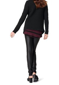 Suéter negro texturizado de manga larga sobre una camiseta a rayas en burdeos y negro, combinado con leggings negros brillantes y zapatos de tacón alto.