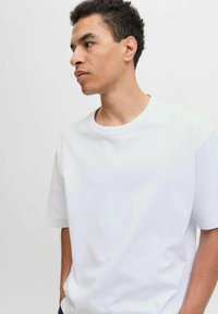 Tricou alb din bumbac, cu guler rotund, mâneci scurte și croială lejeră. Textură netedă, design simplu, fără modele sau grafică vizibile.