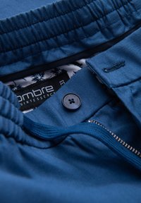 Shorts en tissu bleu avec une taille élastique, une fermeture éclair et un bouton. L'intérieur est doublé d'un motif florale.