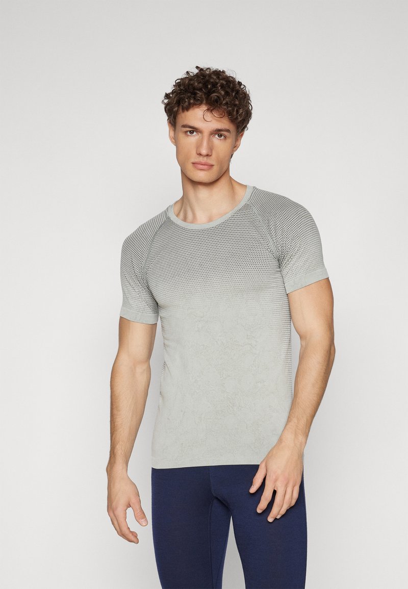 Camiseta atlética de manga curta cinza-claro com padrão texturizado, decote redondo e silhueta ajustada, combinada com leggings azul-escuro.