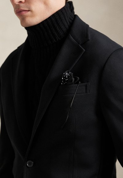 Μαύρο δομημένο σακάκι πάνω από μαύρο ριμπ πλεκτό ζιβάγκο, με μαντηλάκι τσέπης με λευκές πουά βούλες. Λείο ύφασμα και ραμμένη εφαρμογή.