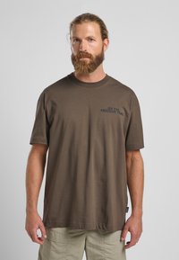 Bruine katoenen t-shirt met korte mouwen, voorzien van blauwe tekst "ON THE FREEDOM TRAIL" op de linkerborst. Ronde halslijn, ontspannen pasvorm.