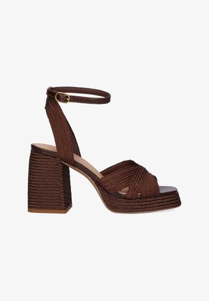 Sandalia marrón tejida con tacón bloque, tira en el tobillo y hebilla, con tiras cruzadas sobre los dedos abiertos y suela plataforma texturizada.