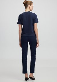 Námořnická modrá košile s krátkým rukávem a kulatým výstřihem, doplněná o slim fit námořnické kalhoty, nošené s černými podpatky.