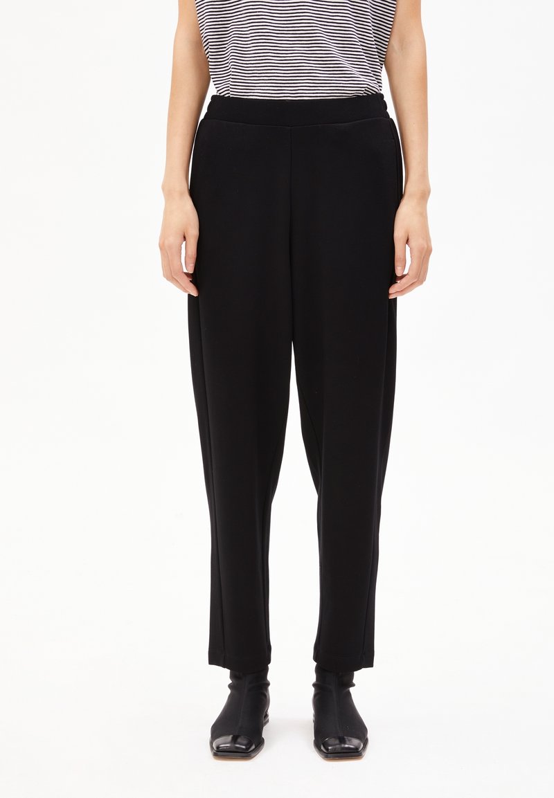 Black, loose-fitting trousers with a smooth texture and elastic waistband. Worn with fitted black ankle boots and a striped top.