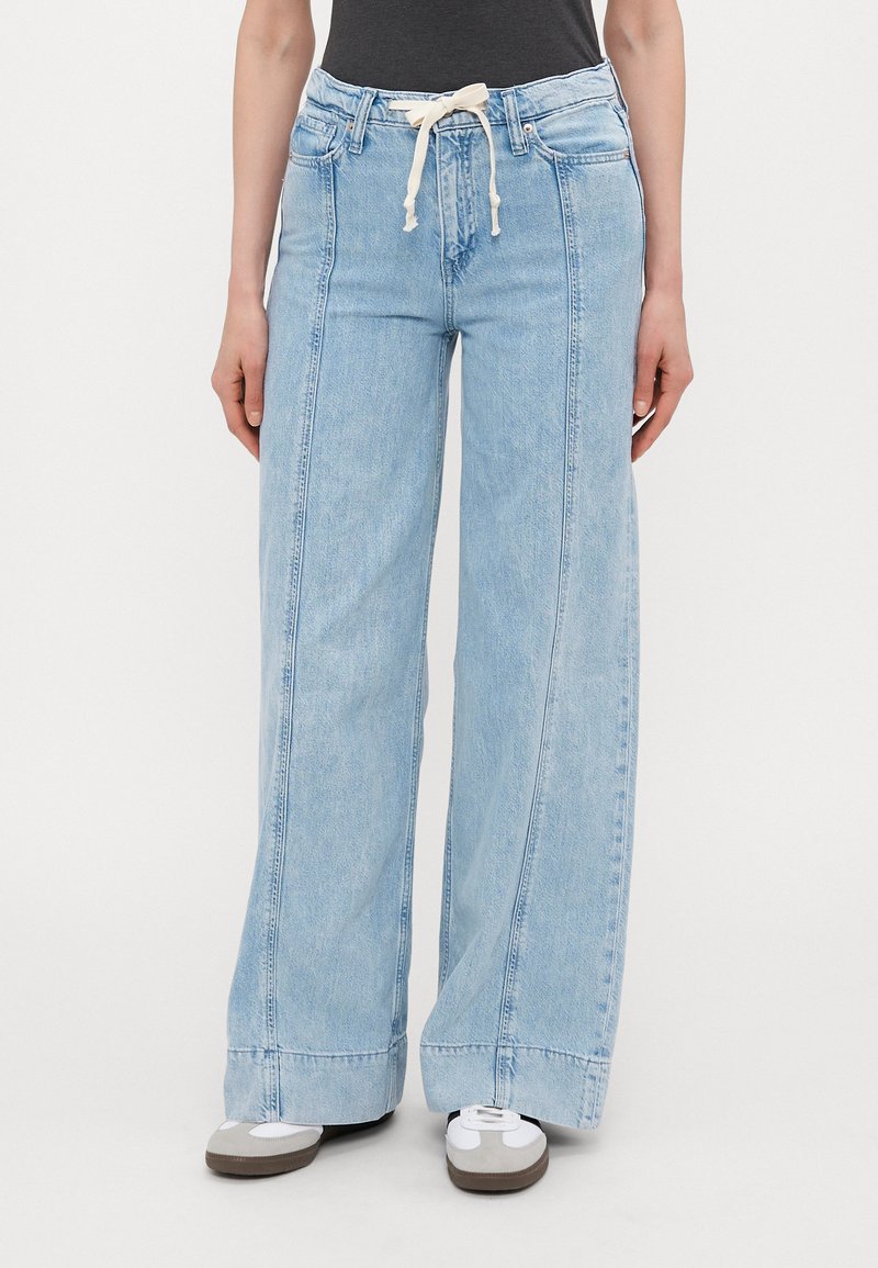 Lys blå vide jeans med snøring i livet og sidelommer, laget av denimstoff med en falmet finish og dobbelt søm detaljer.