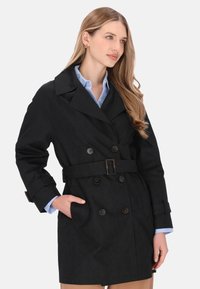 Trenci negru cu dublu pieptăn cu curea, prevăzut cu nasturi mari și material texturat. Stilizat cu o cămașă bleu deschis dedesubt.