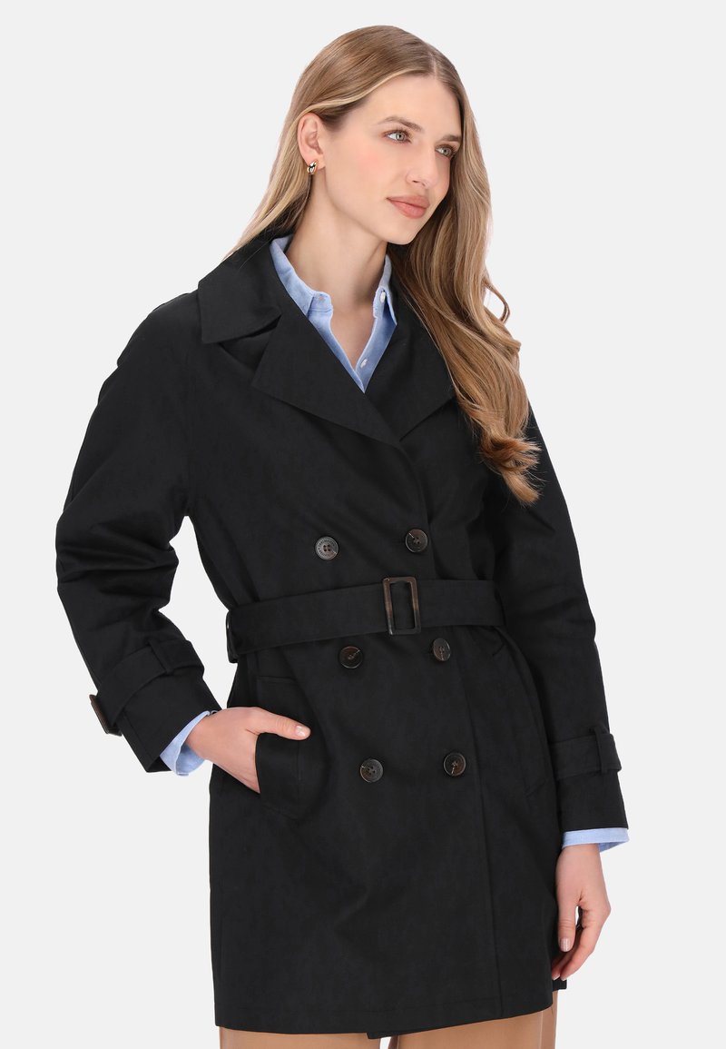 Trenci negru cu dublu pieptăn cu curea, prevăzut cu nasturi mari și material texturat. Stilizat cu o cămașă bleu deschis dedesubt.