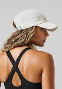 Biała bawełniana czapka z zakrzywionym daszkiem, regulowanym paskiem z tyłu i czarnym logo z przodu. Czarny sportowy top bez rękawów z krzyżowym stylem na plecach.