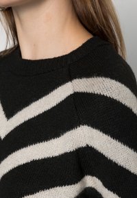 Pull noir et crème à rayures avec une coupe décontractée, présentant un col rond et un tissu tricoté doux et texturé.