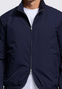 Donkerblauw jack met rits, gemaakt van gladde stof, voorzien van een opstaande kraag, elastische zoom en zijzakken, met een metalen ritssluiting als detail.