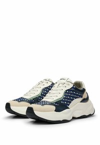 Shoe in navy and cream with fabric upper, textured pattern, padded tongue, and rubber outsole. Features brand logo on tongue.